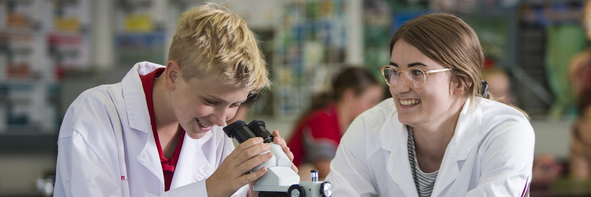 Two students wearing lab coats and using a microscope
