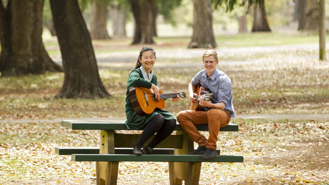 Two students outside playing guitars