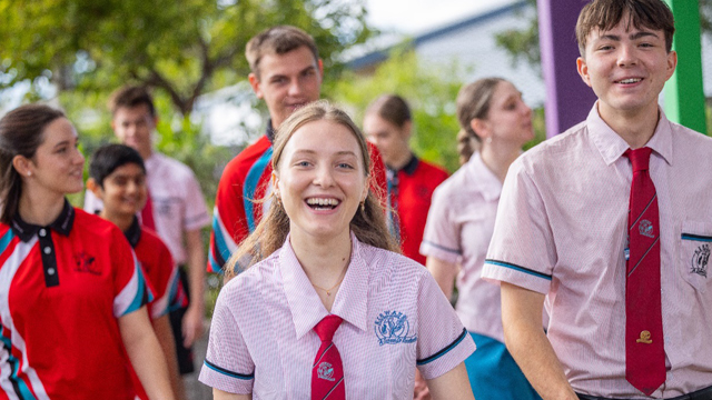 Students outdoors in their school uniforms. Students in a sports uniform in the background.