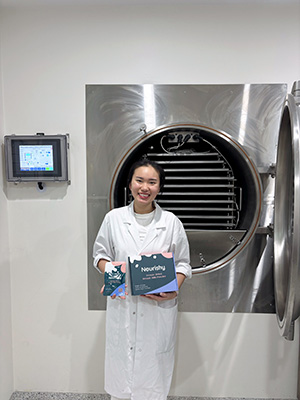 Bailey in a lab coat holding a freeze-dried breast milk powder product called Nourishy..
